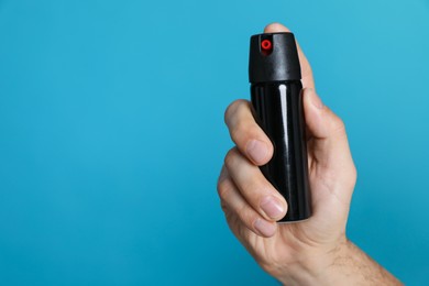 Photo of Man using pepper spray on turquoise background, closeup. Space for text