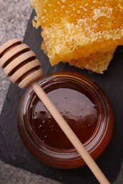 Photo of Sweet golden honey in jar, dipper and pieces of honeycomb on grey table, top view