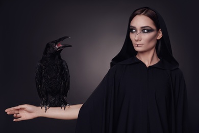 Photo of Mysterious witch with raven on dark background