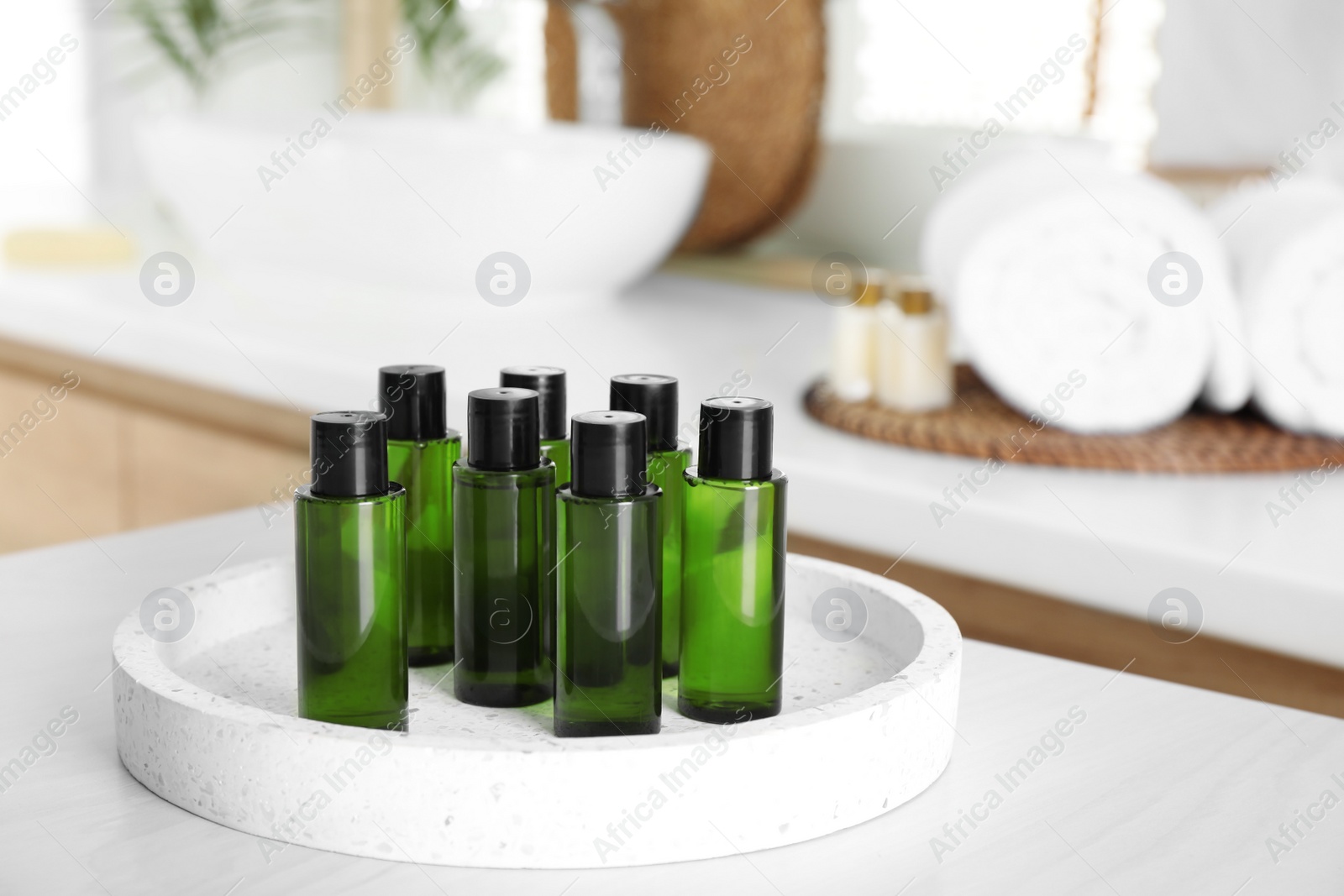 Photo of Mini bottles with cosmetic products on white table in bathroom