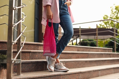 Photo of Young woman with stylish pink net bag on stairs outdoors, closeup