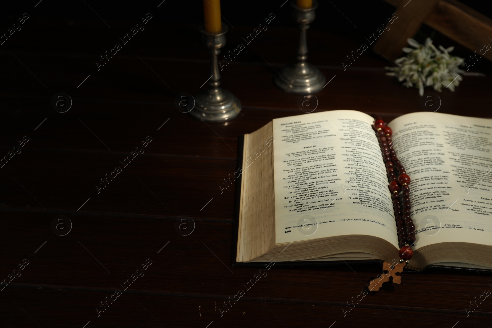 Photo of Cross, rosary beads, Bible and church candle on wooden table, space for text