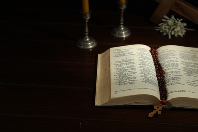 Photo of Cross, rosary beads, Bible and church candle on wooden table, space for text
