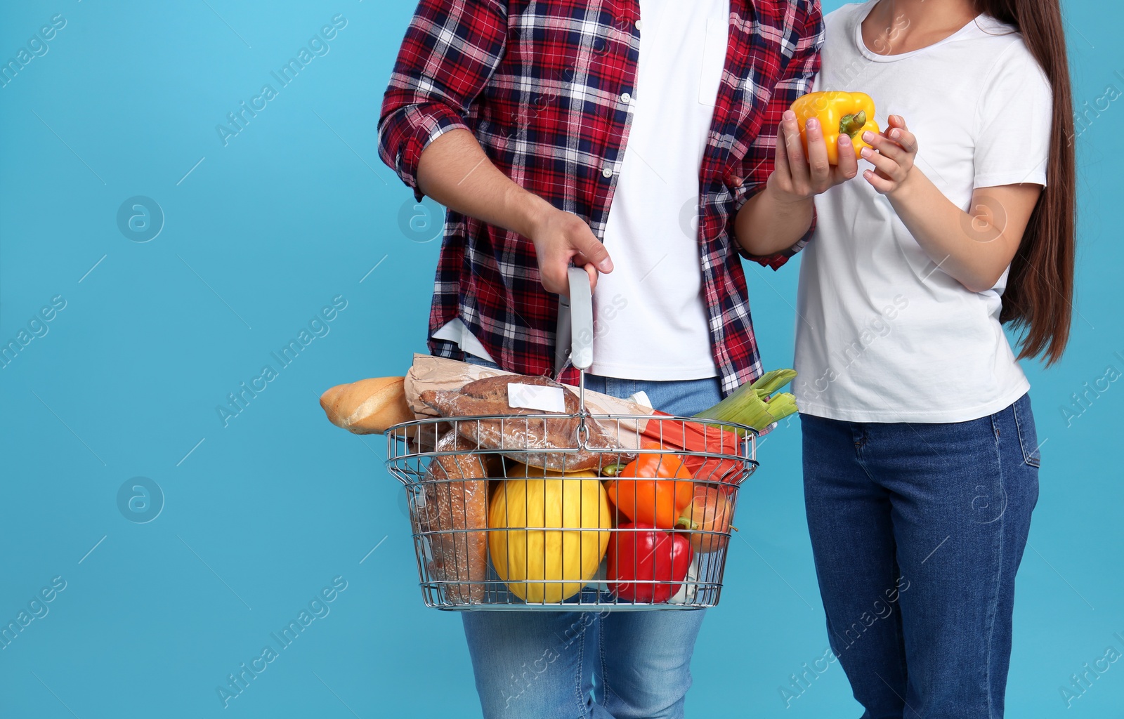 Photo of Young couple with shopping basket full of products on blue background, closeup