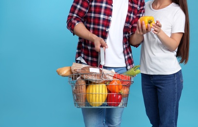 Photo of Young couple with shopping basket full of products on blue background, closeup