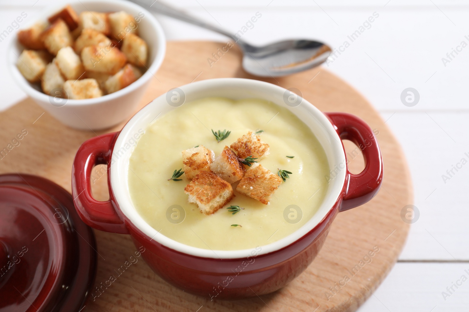 Photo of Tasty potato soup with croutons and rosemary in ceramic pot on white table, closeup