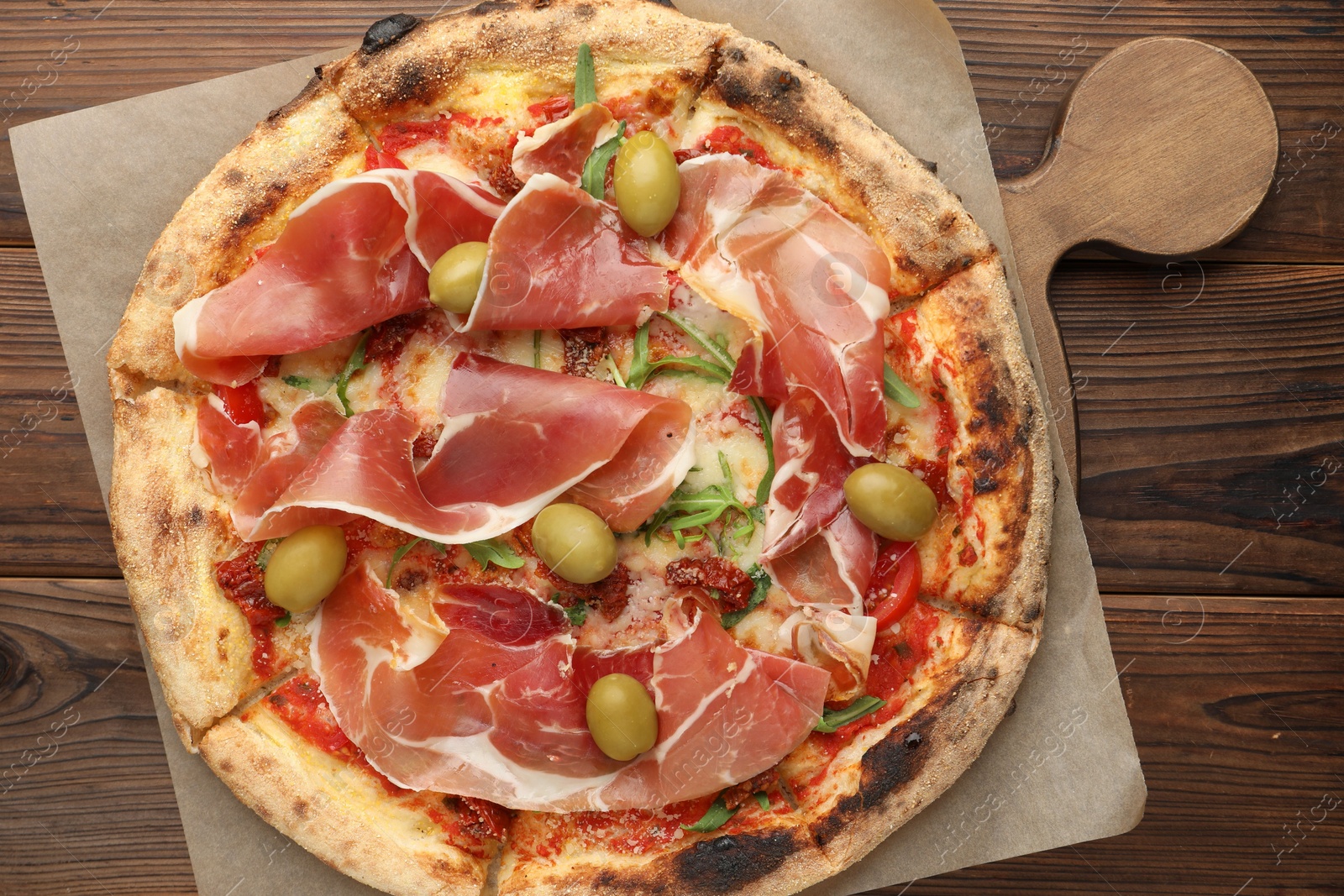 Photo of Tasty pizza with cured ham, olives and sun-dried tomato on wooden table, top view