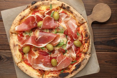 Photo of Tasty pizza with cured ham, olives and sun-dried tomato on wooden table, top view