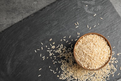 Photo of Slate plate with raw unpolished rice in bowl on table, top view. Space for text