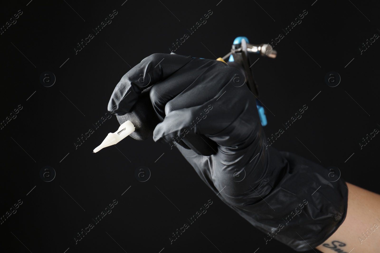 Photo of Professional tattoo artist with machine on black background, closeup