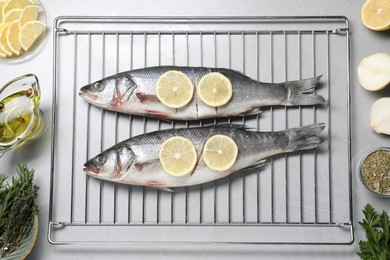 Photo of Oven rack with raw sea bass fish and ingredients on light grey table, flat lay