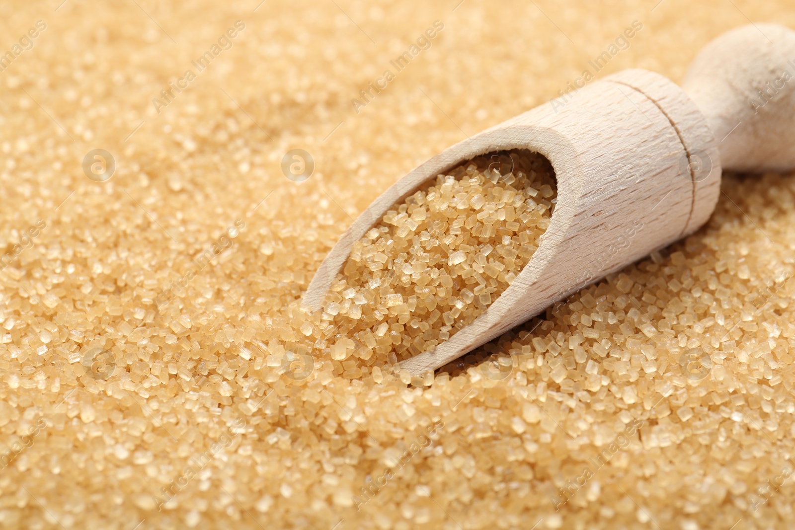 Photo of Wooden scoop on granulated brown sugar, closeup view