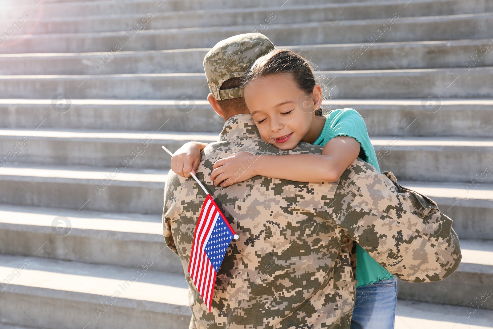 Photo of Soldier and his little daughter with flag of USA hugging outdoors, space for text