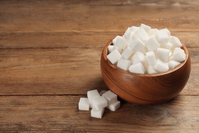 Photo of Bowl and white sugar cubes on wooden table. Space for text