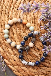 Photo of Beautiful bracelets with gemstones and lavender on wicker mat, flat lay