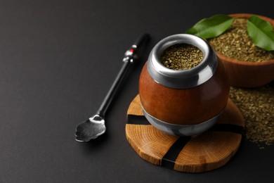 Photo of Calabash with mate tea and bombilla on black table. Space for text