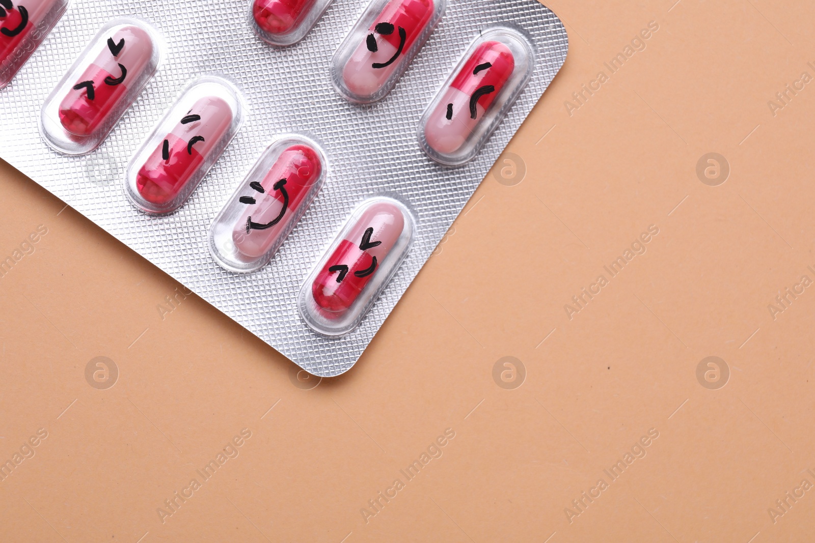 Photo of Blister of antidepressant pills with emotional faces on pale orange background, top view. Space for text