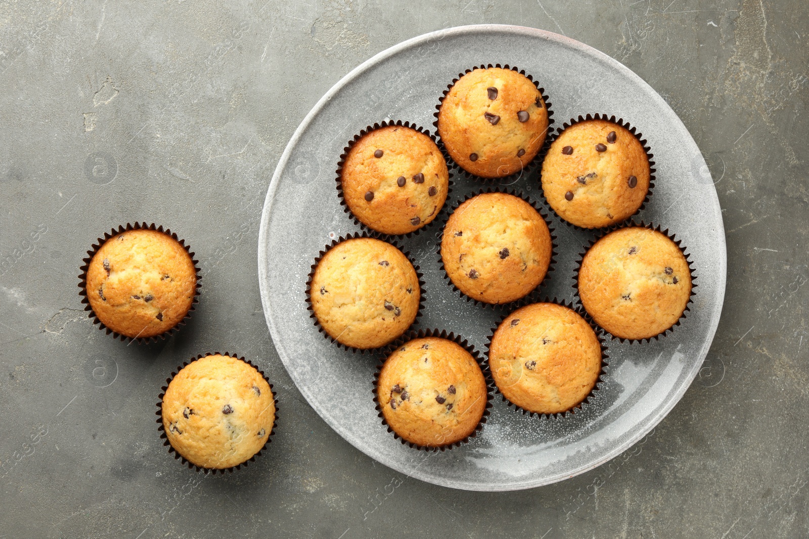 Photo of Delicious freshly baked muffins with chocolate chips on gray table, top view