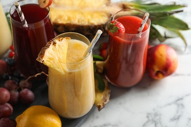 Photo of Glasses of delicious juices and fresh ingredients on white marble table, closeup