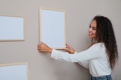 Photo of Happy African American woman hanging empty frame on pale rose wall in room. Mockup for design