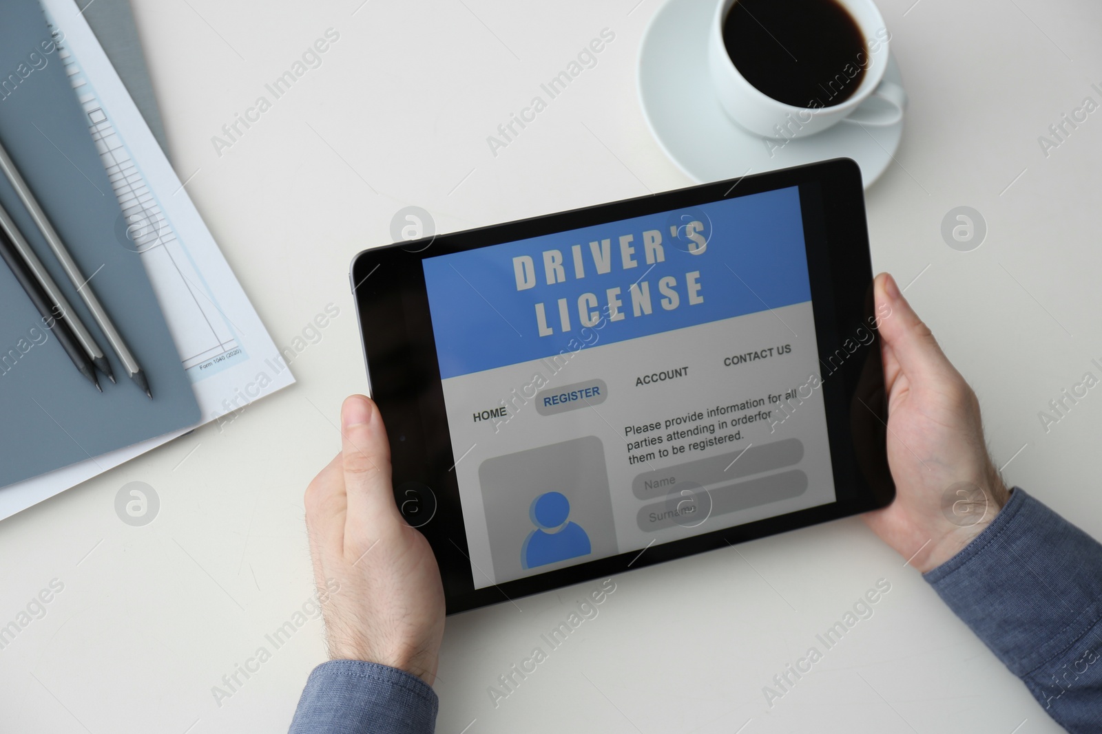 Photo of Man holding tablet with driver's license application form at white table, above view