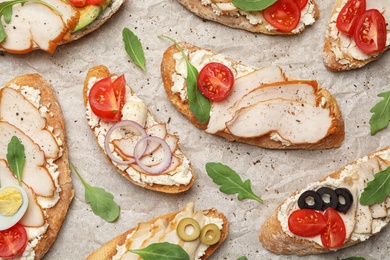 Photo of Different delicious chicken bruschettas on parchment, flat lay