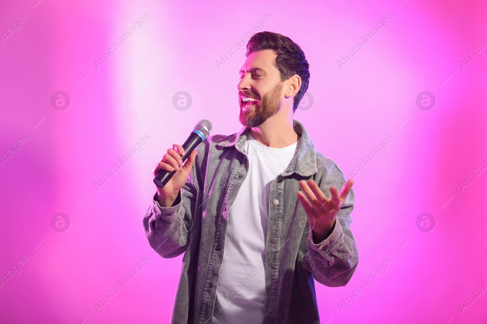 Photo of Handsome man with microphone singing on pink background