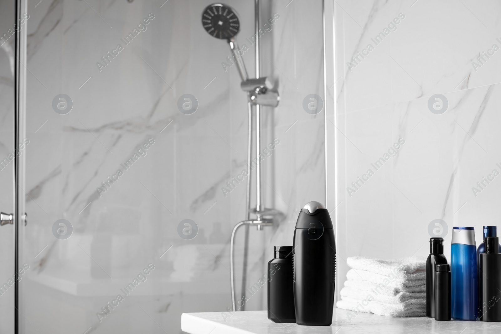 Photo of Shampoo, conditioner, other toiletries and towels on white table near shower stall in bathroom, space for text