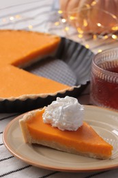 Piece of fresh homemade pumpkin pie served with whipped cream and tea on table