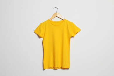 Photo of Hanger with yellow t-shirt on light wall. Mockup for design