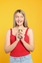 Beautiful woman drinking from beverage can on yellow background