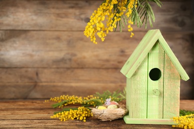 Stylish bird house, nest and fresh mimosas on wooden background. Space for text