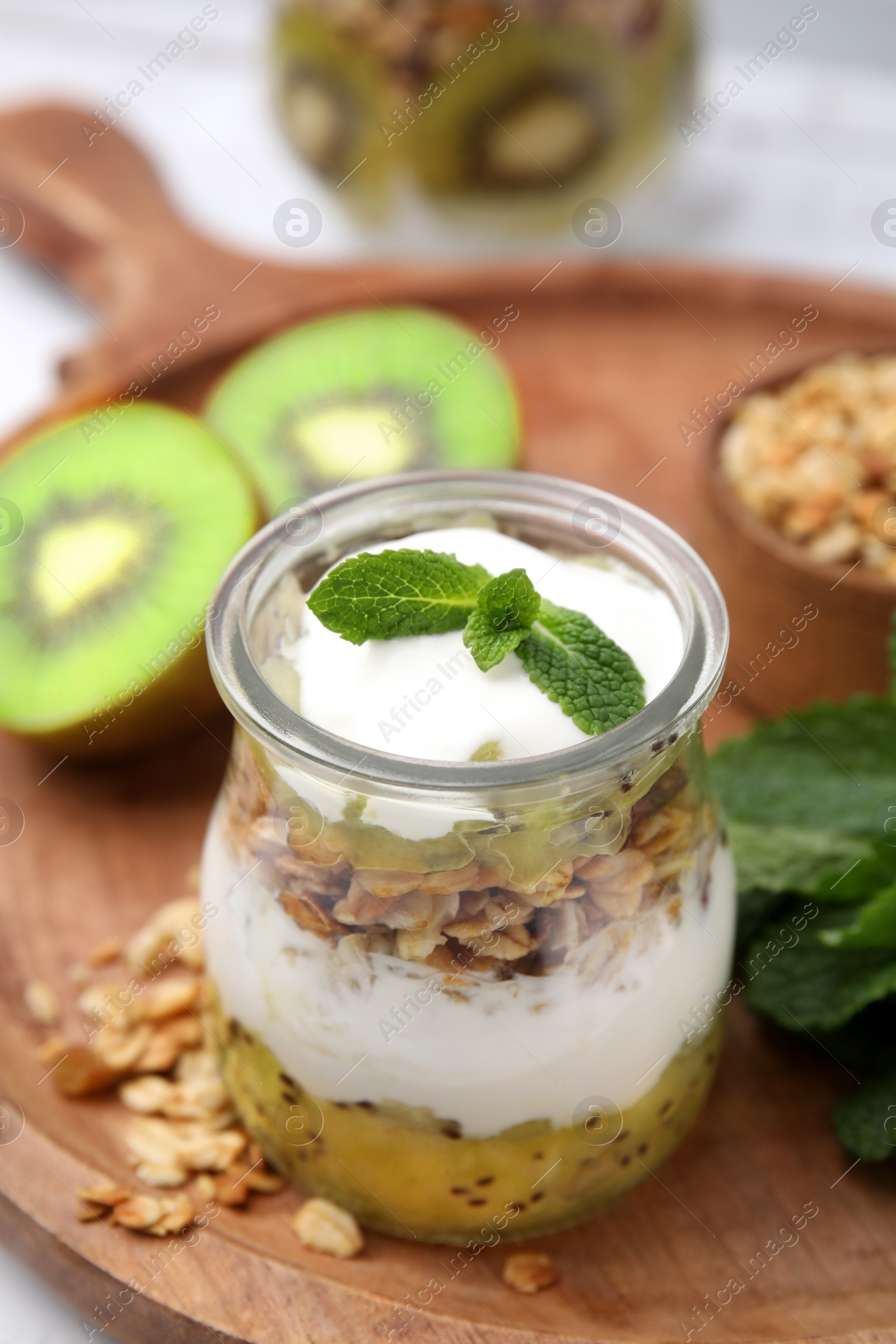 Photo of Delicious dessert with kiwi, yogurt and muesli on wooden board, closeup