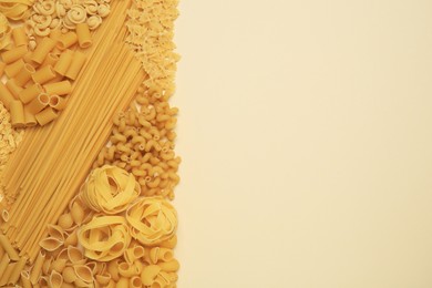 Different types of pasta on beige background, flat lay. Space for text