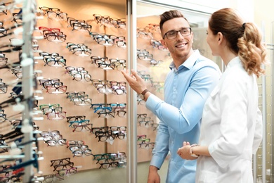 Female ophthalmologist helping man to choose glasses in optical store