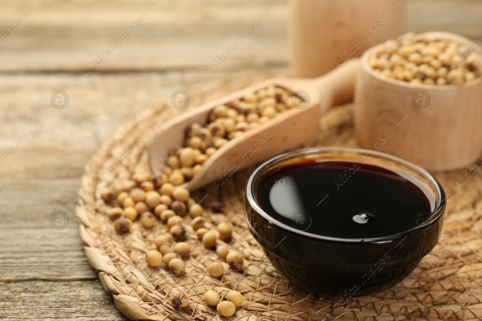 Photo of Soy sauce in bowl and beans on wooden table, closeup. Space for text