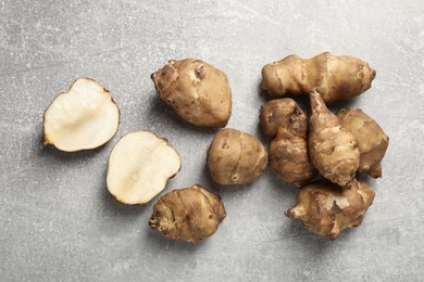 Whole and cut Jerusalem artichokes on light grey table, flat lay