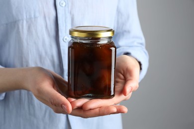 Photo of Woman holding jar of tasty sweet fig jam on grey background, closeup. Space for text