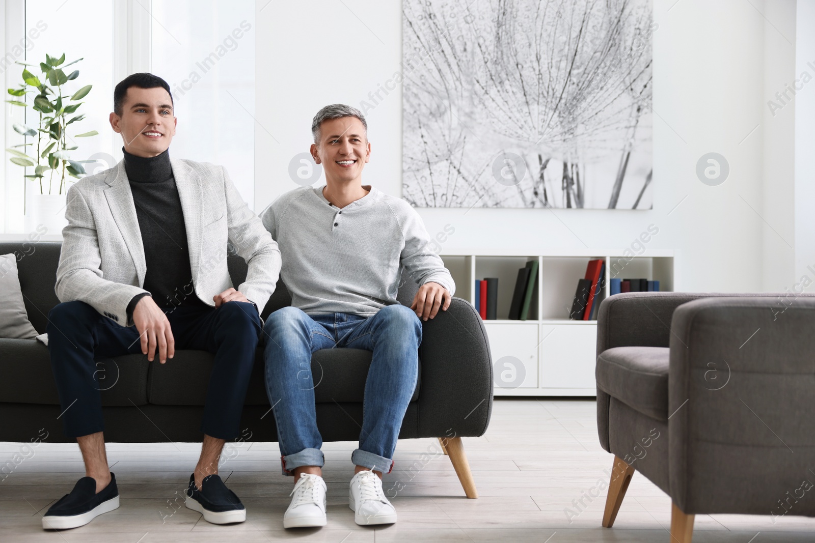 Photo of Happy men sitting on sofa at home