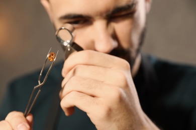 Photo of Male jeweler evaluating precious gemstone in workshop, closeup