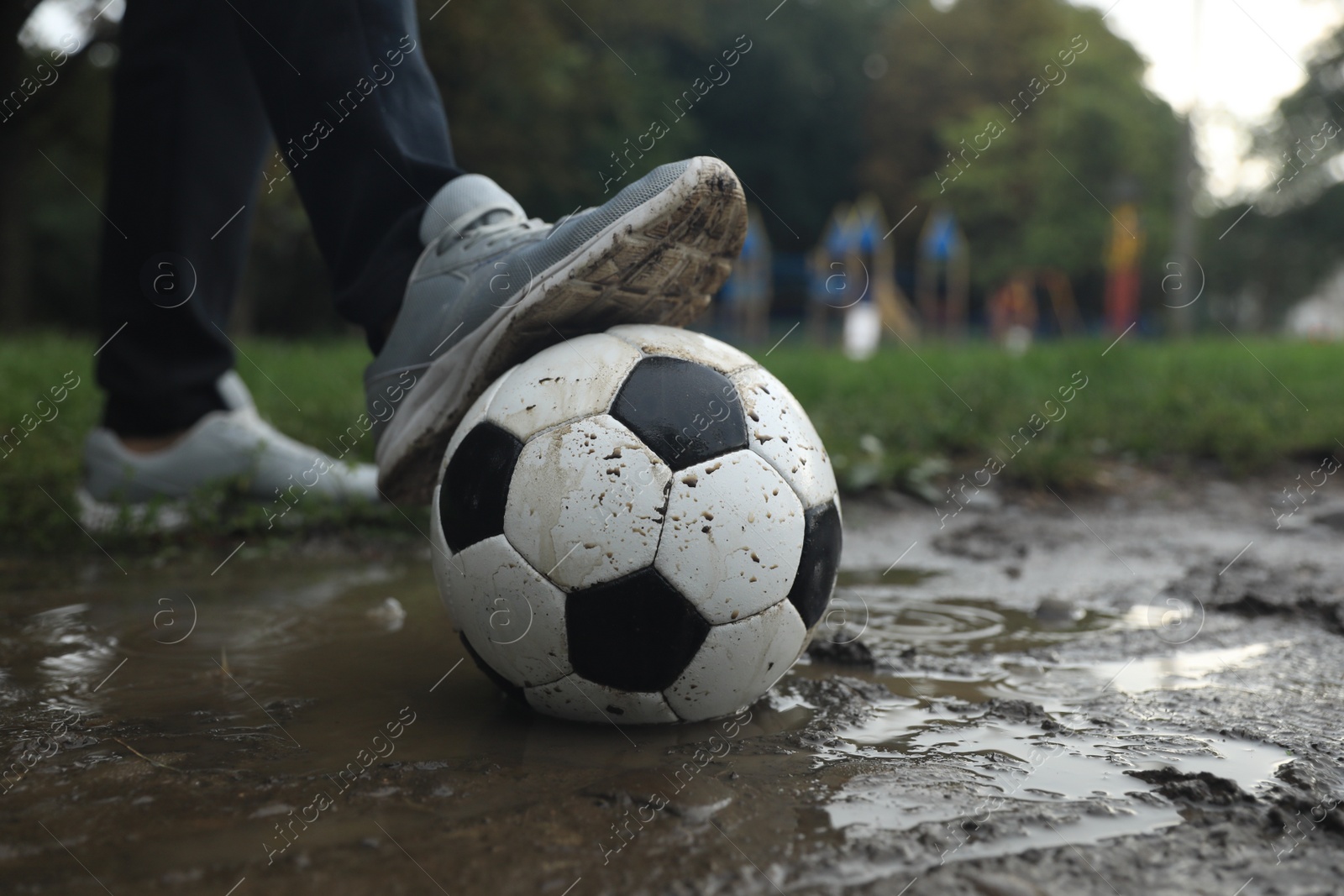 Photo of Man with dirty soccer ball in puddle outdoors, closeup