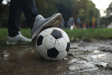 Man with dirty soccer ball in puddle outdoors, closeup