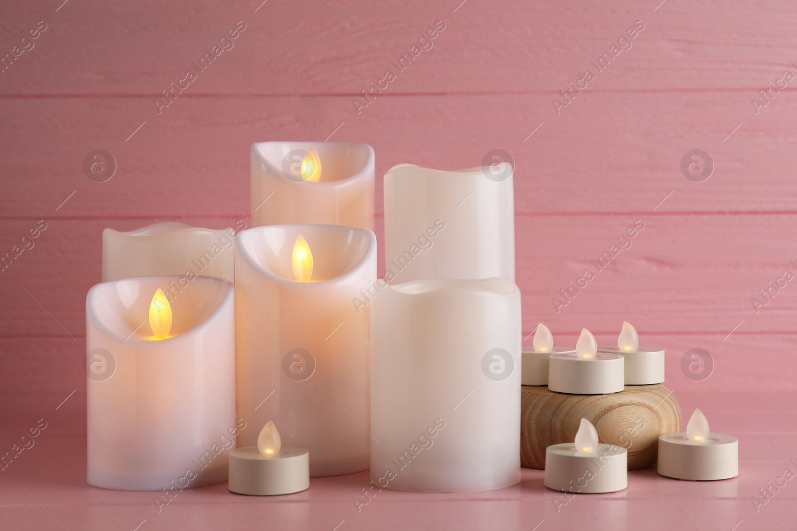 Photo of Glowing decorative LED candles on pink wooden background