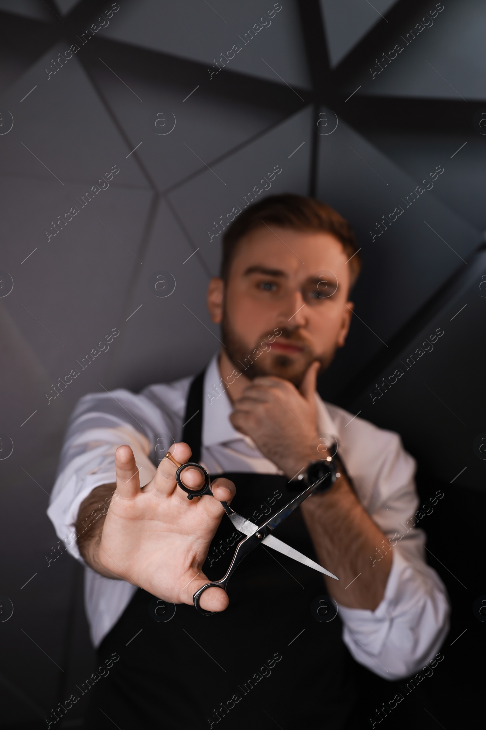 Photo of Hairdresser near dark wall, focus on professional scissors