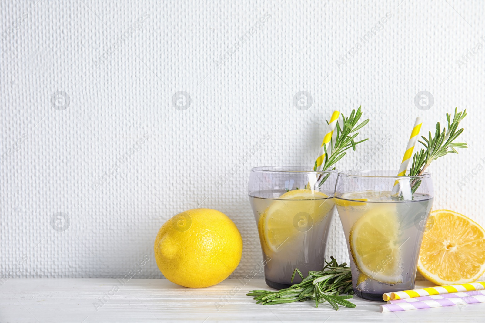 Photo of Glasses of fresh lemon cocktail with rosemary and space for text on light background