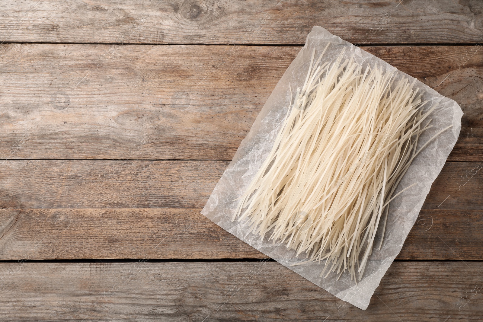 Photo of Raw rice noodles on wooden background, top view. Space for text