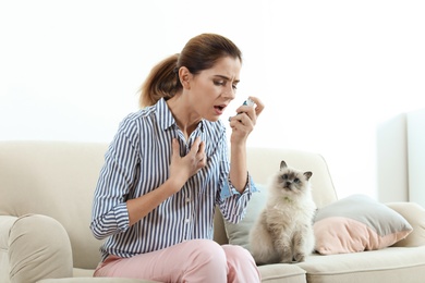 Woman using asthma inhaler near cat at home. Health care
