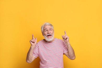 Photo of Senior man with mustache pointing at something on orange background