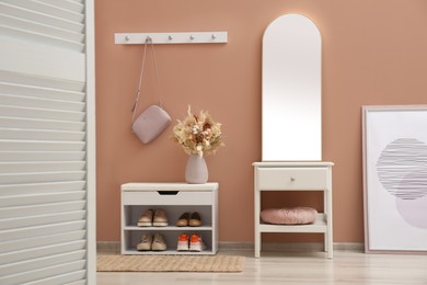 Hallway interior with mirror and white furniture near light pink wall. Stylish accessories