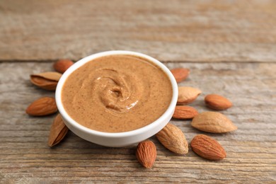 Photo of Delicious nut butter in bowl and almonds on wooden table, closeup